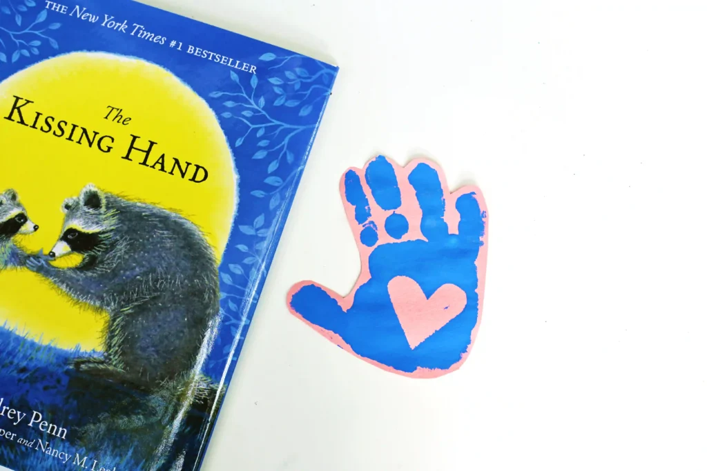 a blue handprint with a heart in the middle on pink paper next to a book