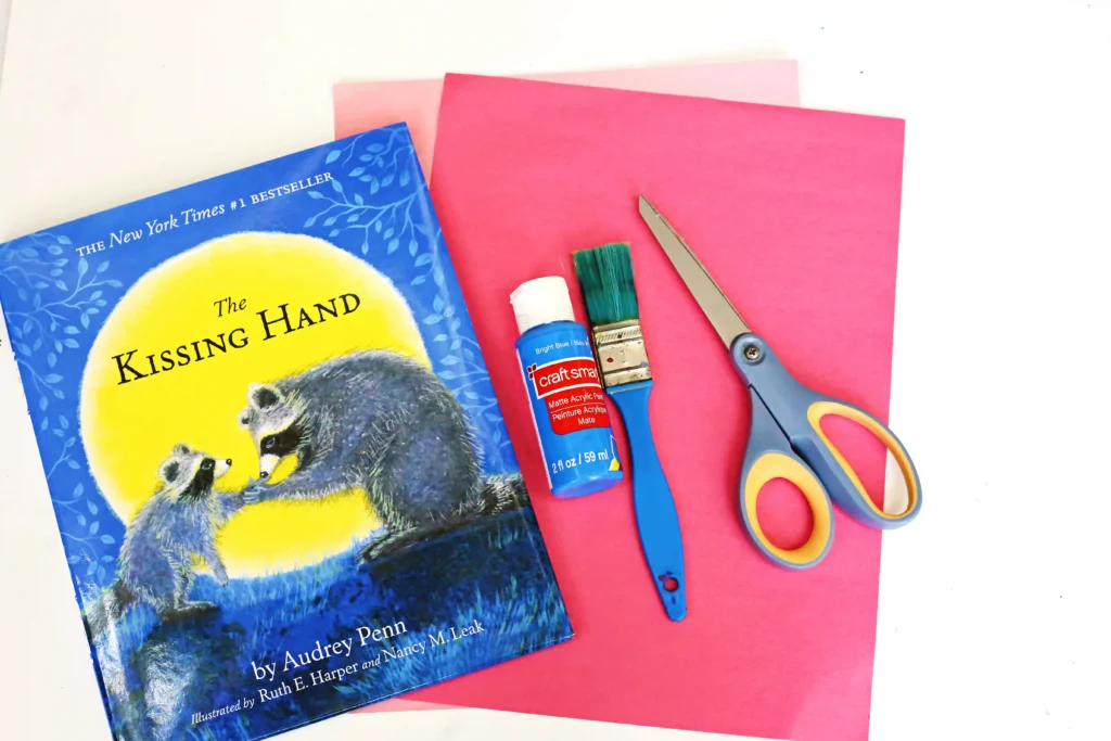 supplies for the kissing hand handprint craft: blue paint, a paintbrush, scissors, and pink and red construction paper
