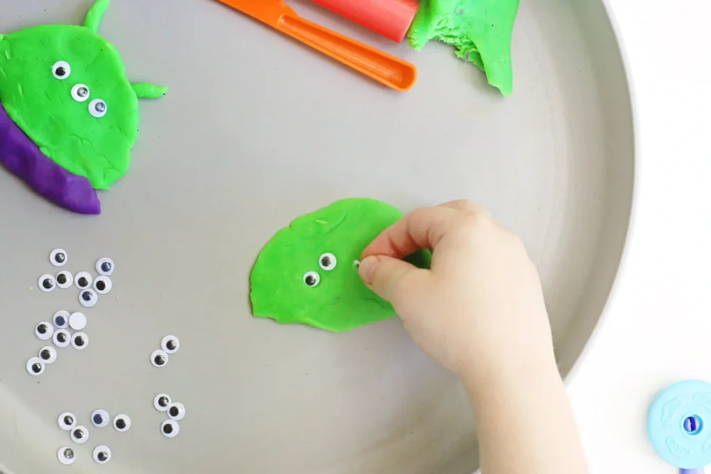a kid putting googly eyes on playdough to make an alien
