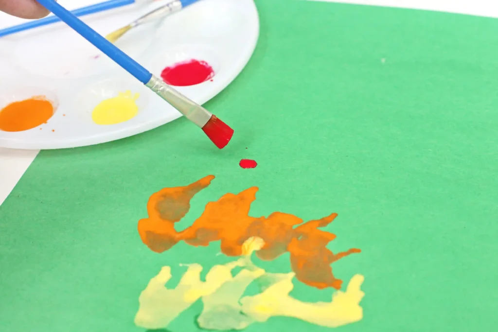 a paintbrush dropping red paint on a green piece of paper
