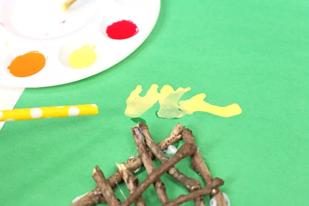 a kid using a straw to blow yellow paint across green paper