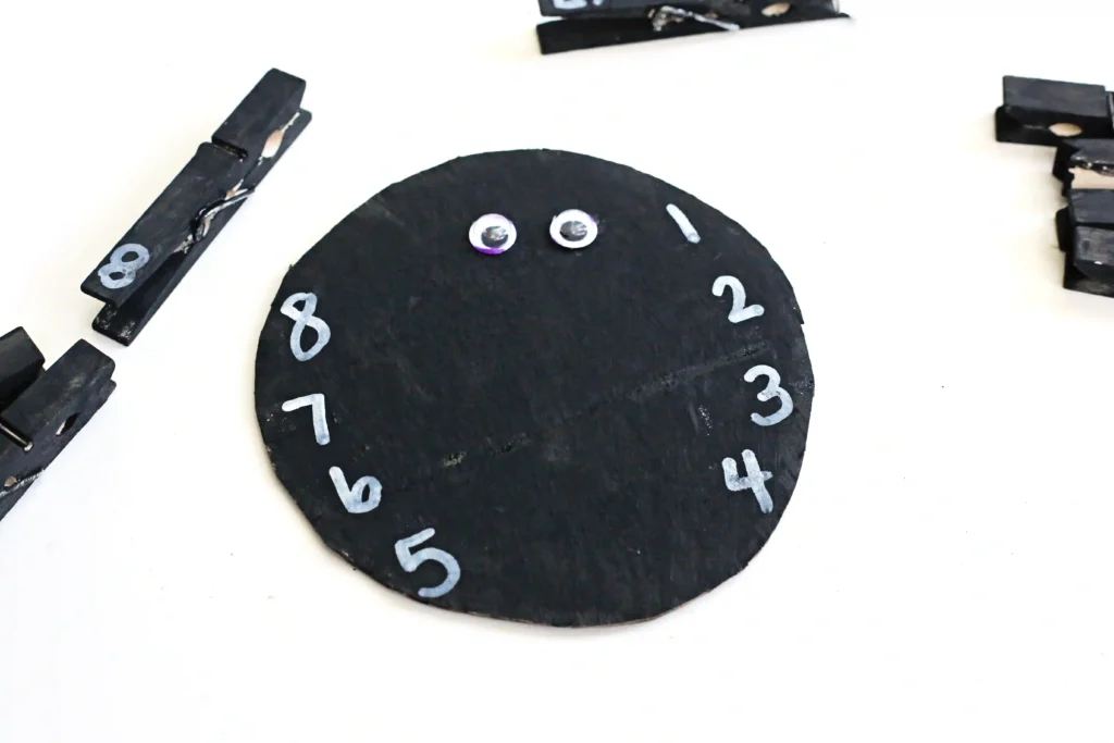 cardboard cut into a circle and painted black with googly eyes and numbers written on it