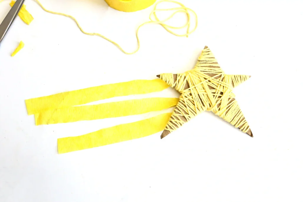 a Yarn-Wrapped Shooting Star Craft that is cardboard cut into a star and wrapped with yellow yarn and has yellow streamers attached