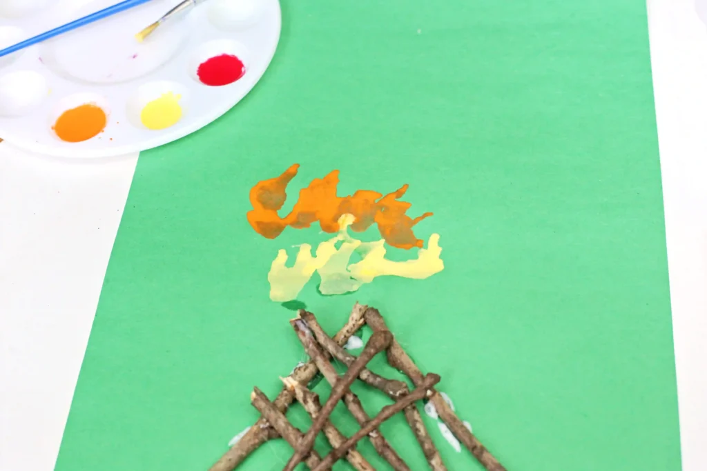 a green piece of construction paper with sticks glued on and yellow and orange paint made to look like a fire