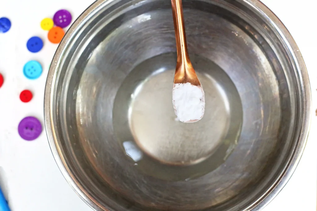 baking soda being added to warm water and clear school glue in a bowl