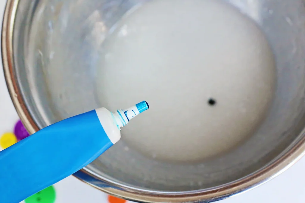 blue food dye being added to a bowl of slime