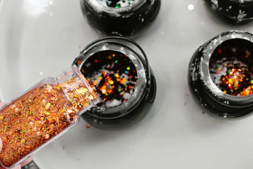orange glitter being added to a cauldron with baking soda and food coloring