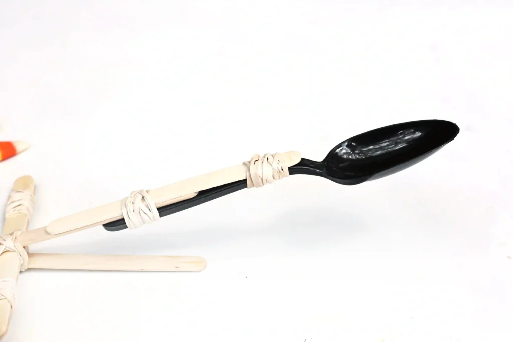 a spoon with popsicle sticks attached using rubber bands