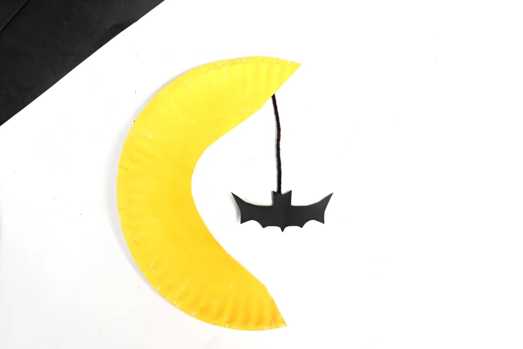 a paper plate cut and painted to look like the moon with a bat hanging down