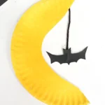 a paper plate cut and painted to look like the moon with a bat hanging down