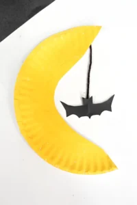 a paper plate cut and painted to look like the moon with a bat hanging down