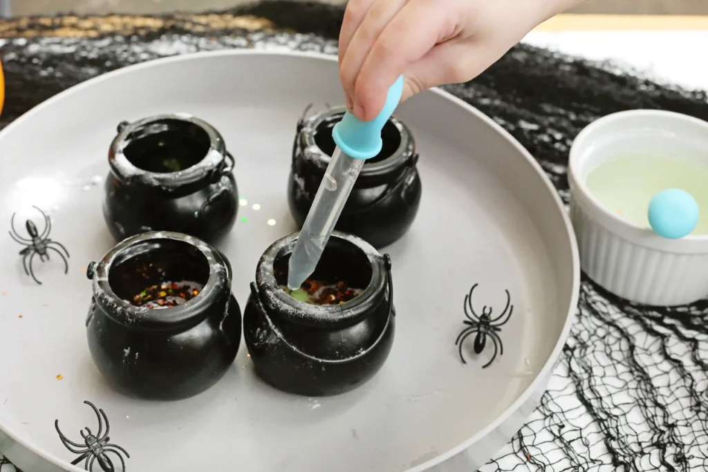 a kid adding vinegar to a cauldron with baking soda and glitter