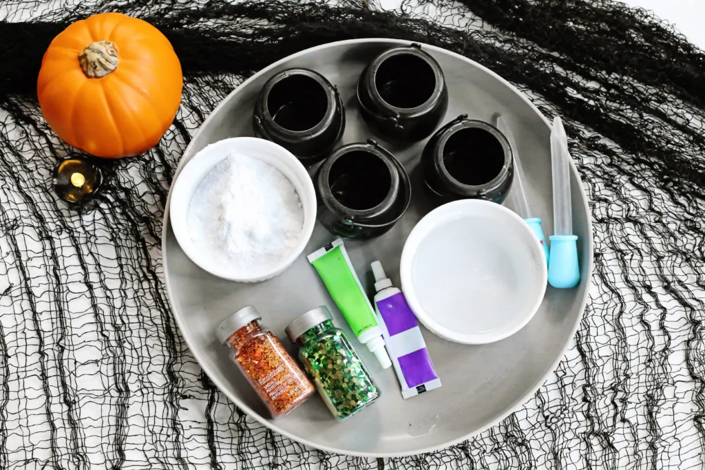 supplies for the bubbling witches brew experiment: cauldrons, baking soda, vinegar, food coloring, and glitter