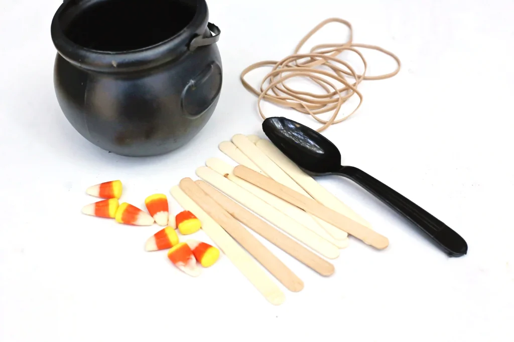supplies for the candy corn catapult: cauldron, candy corn, rubber bands, spoon, and popsicle sticks
