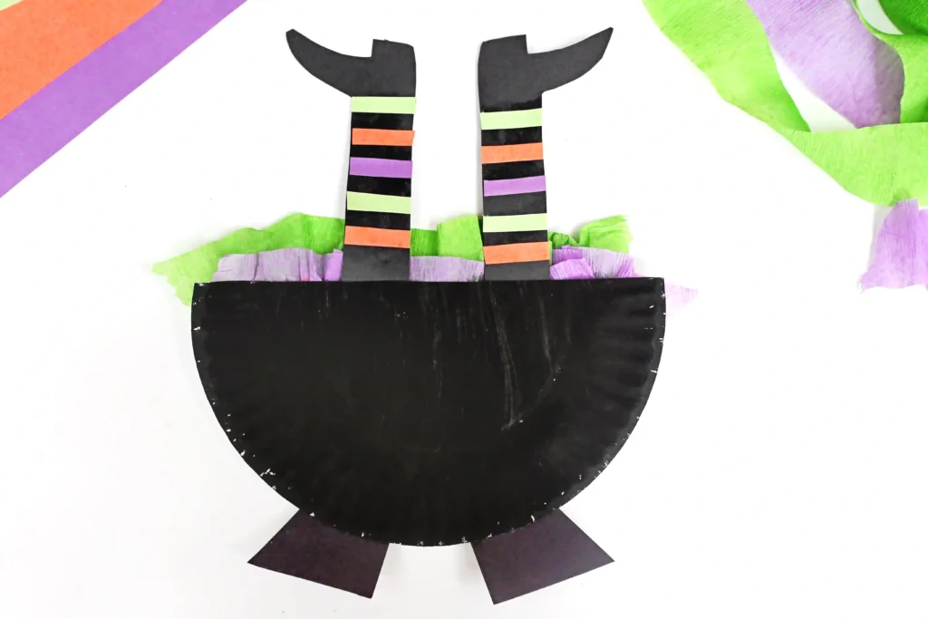 half of a paper plate painted black with witch legs sticking out