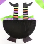 half of a paper plate painted black with witch legs sticking out