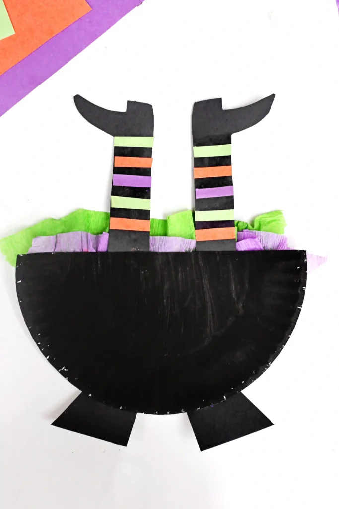half of a paper plate painted black with witch legs sticking out