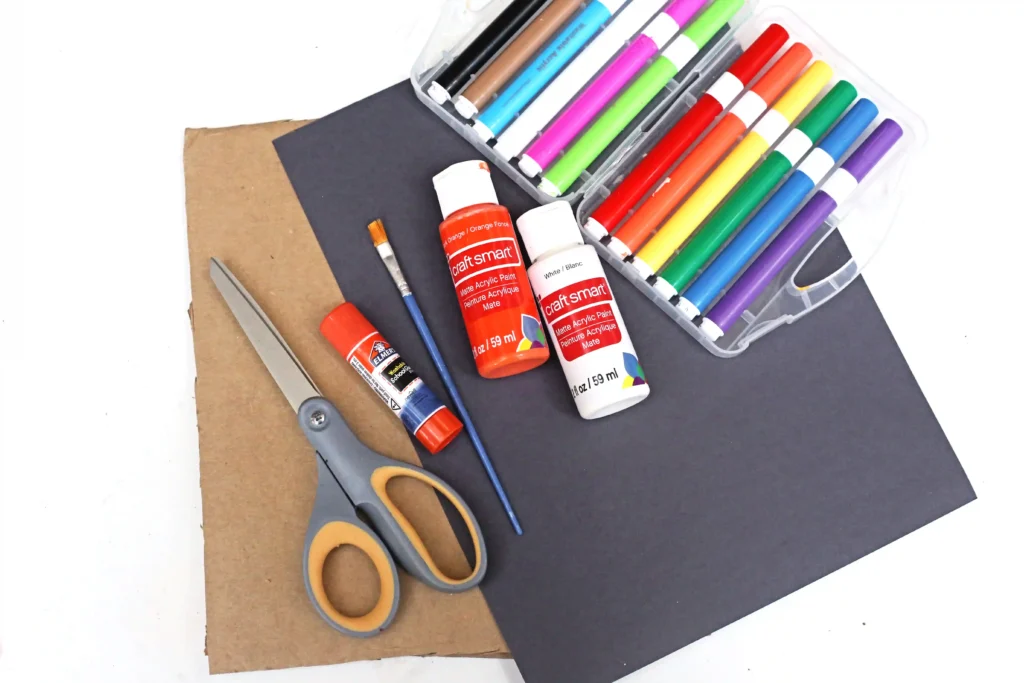 supplies for the ghost family portrait craft: cardboard, black construction paper, orange and white paint, paintbrush, glue, and markers