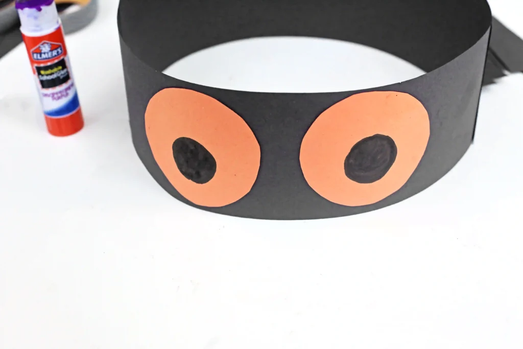 a black construction paper headband with orange eyes