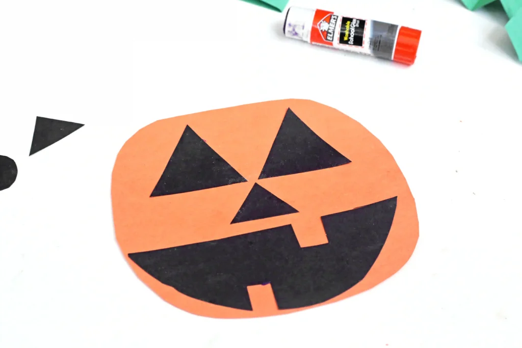 an orange circle cut out of construction paper with a jack-o-lantern face