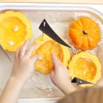 a kid putting pumpkin seeds in a hollowed out pumpkin in water