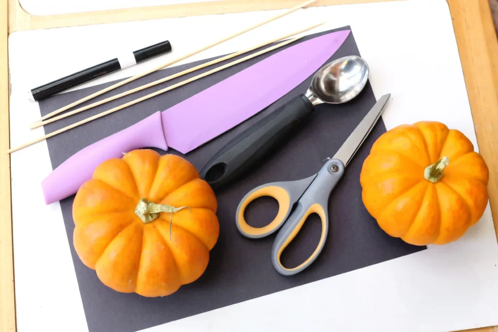 supplies for the halloween boat STEM challenge: mini pumpkins, black paper, a knife, scissors, black marker, and skewers