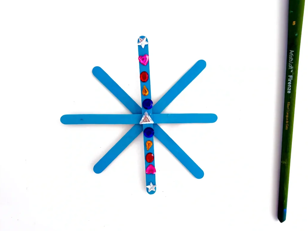 a popsicle stick snowflake with rhinestones glued on