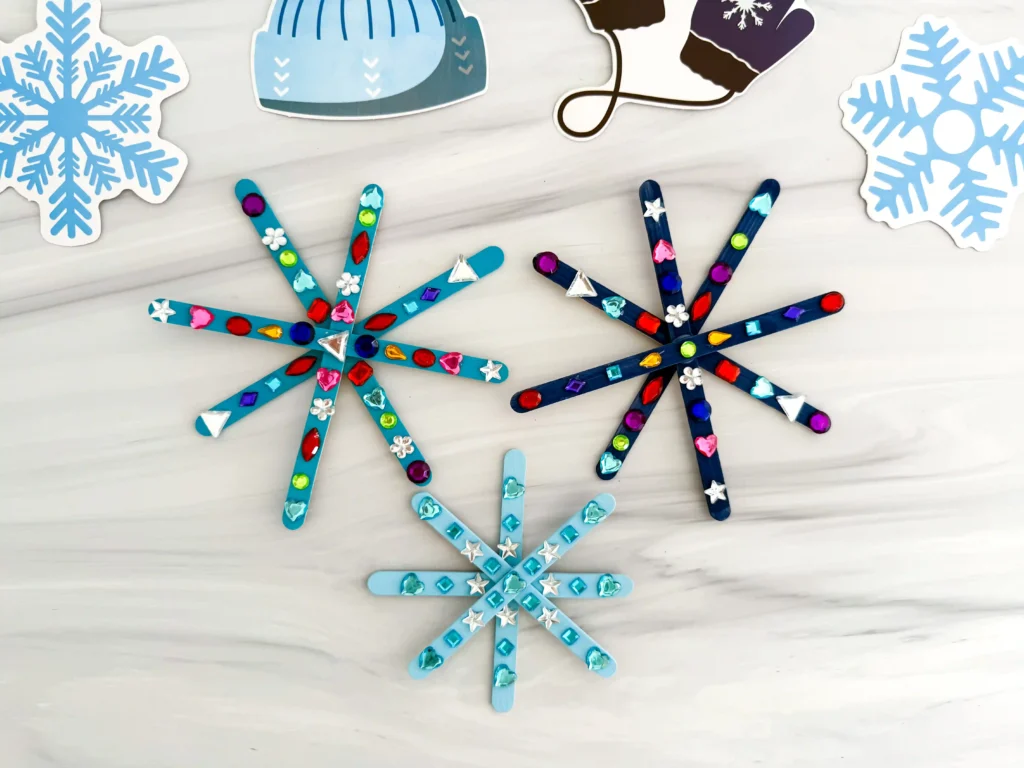 popsicle sticks painted blue and glued together to look like snowflakes with gems on them