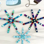 popsicle sticks painted blue and glued together to look like snowflakes with gems on them
