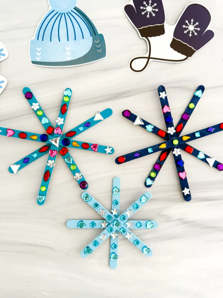 popsicle sticks painted blue and glued together to look like snowflakes with gems on them