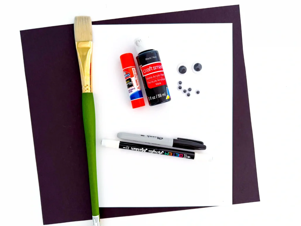 supplies for the spider handprint craft: black paint, a paintbrush, glue, black marker, white marker, and googly eyes