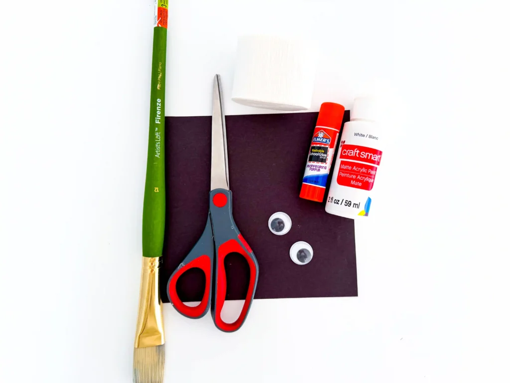 supplies for the mummy handprint craft: black paper, paintbrush, scissors, glue, white paint, and googly eyes