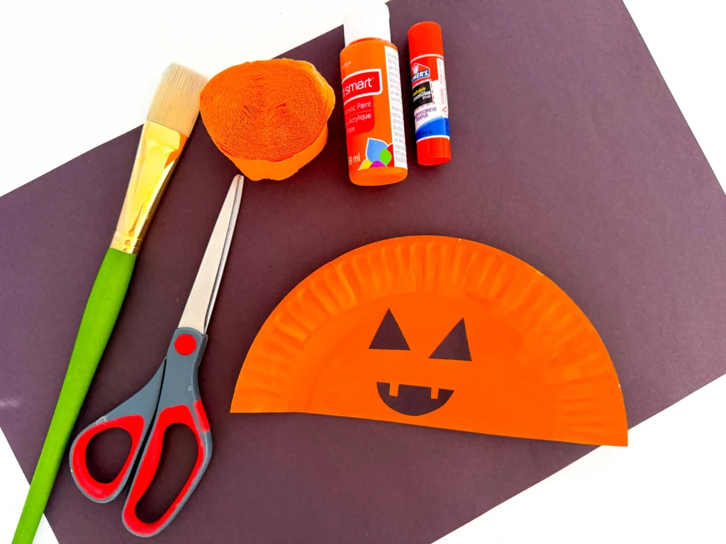 half of a paper plate painted orange with a jack o lantern face