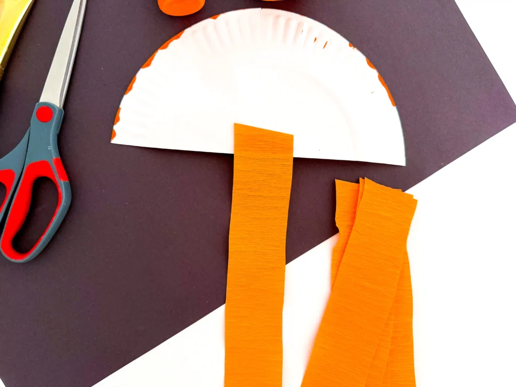orange streamer being glued to the back of half a paper plate