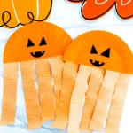 Half a paper plate painted orange with a jack-o-lantern face and orange streamers
