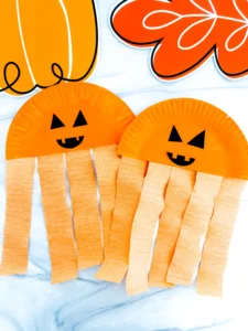 Half a paper plate painted orange with a jack-o-lantern face and orange streamers