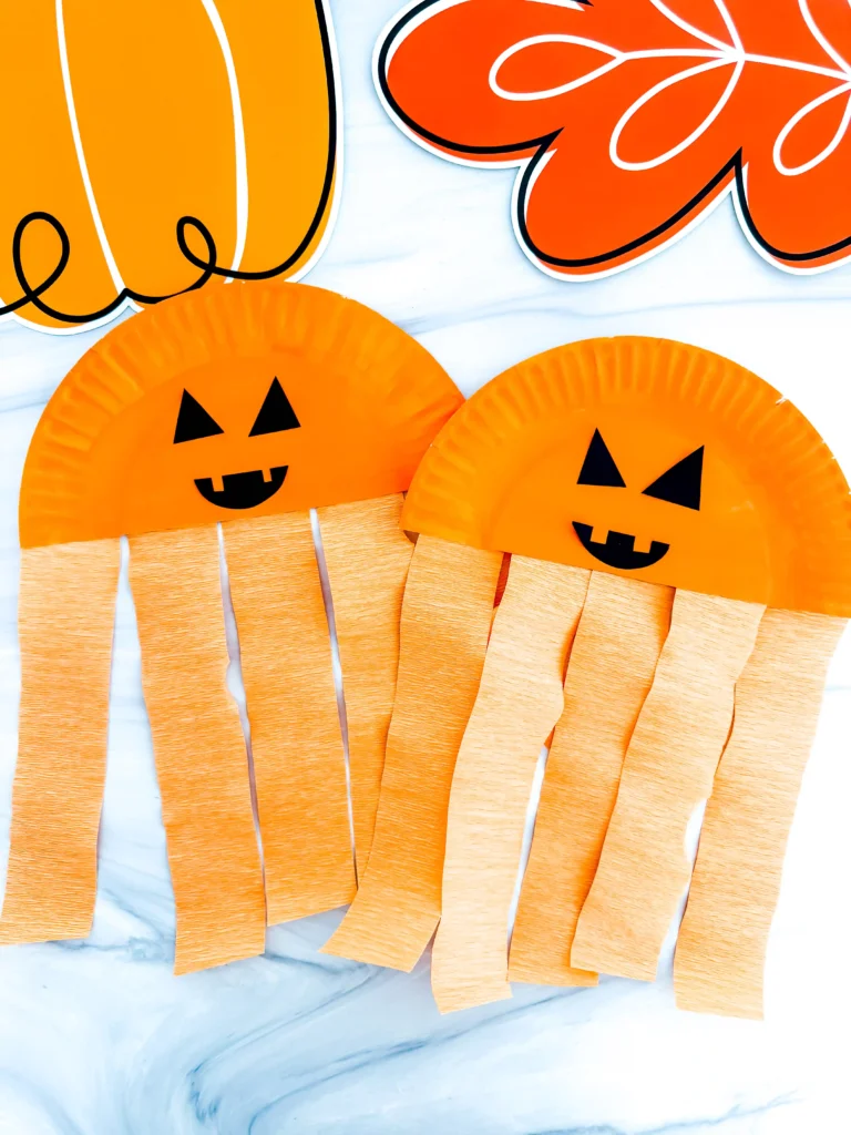 Half a paper plate painted orange with a jack-o-lantern face and orange streamers