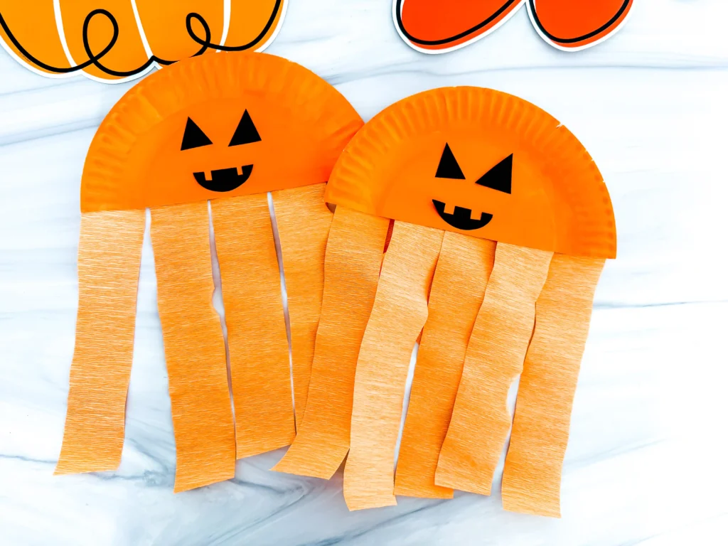 Half a paper plate painted orange with a jack-o-lantern face and orange streamers