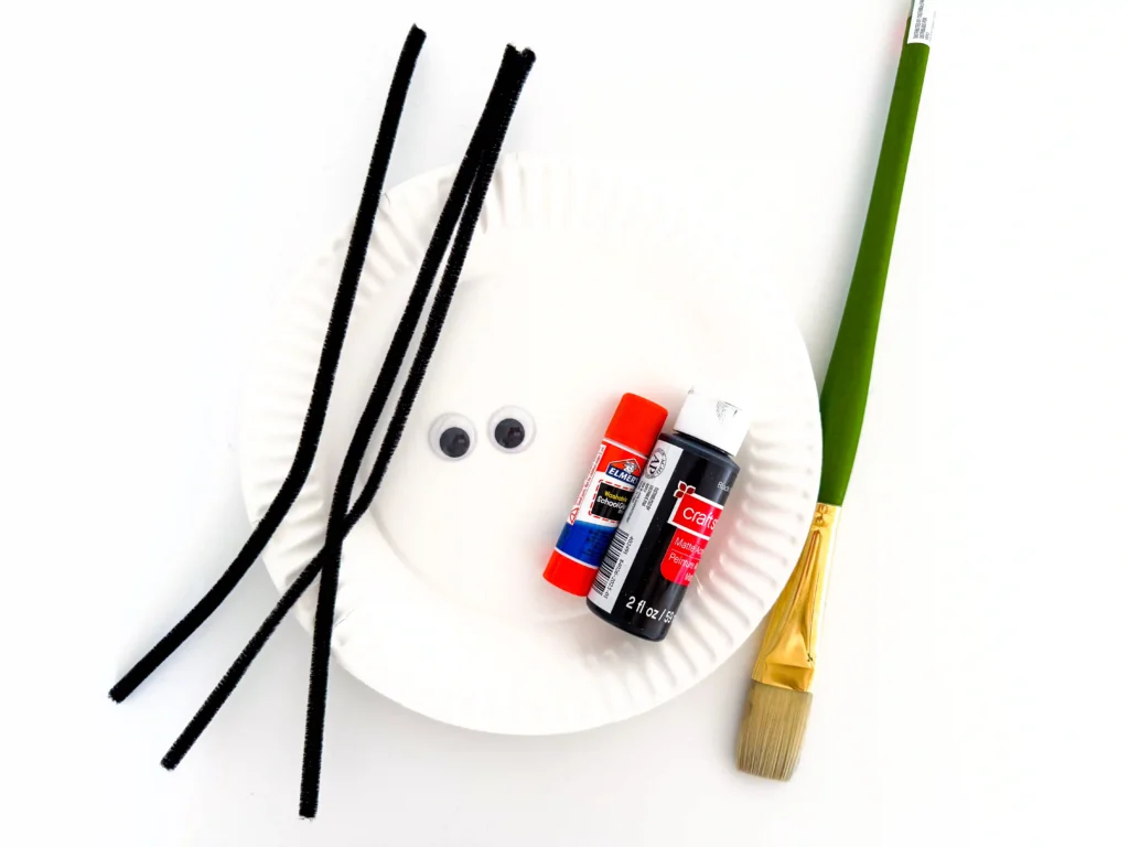 supplies for this spider paper plate craft: black pipe cleaners, googly eyes, paper plate, glue, black paint, and a paint brush.