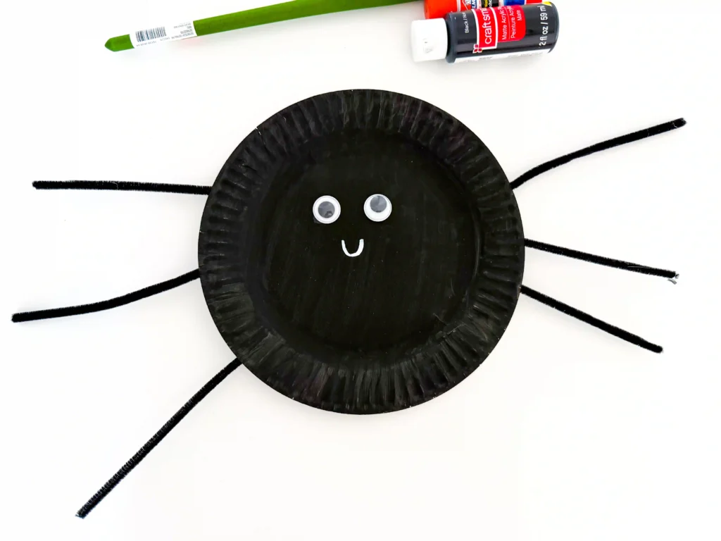 googly eyes glued on a plate painted black with pipe cleaner legs