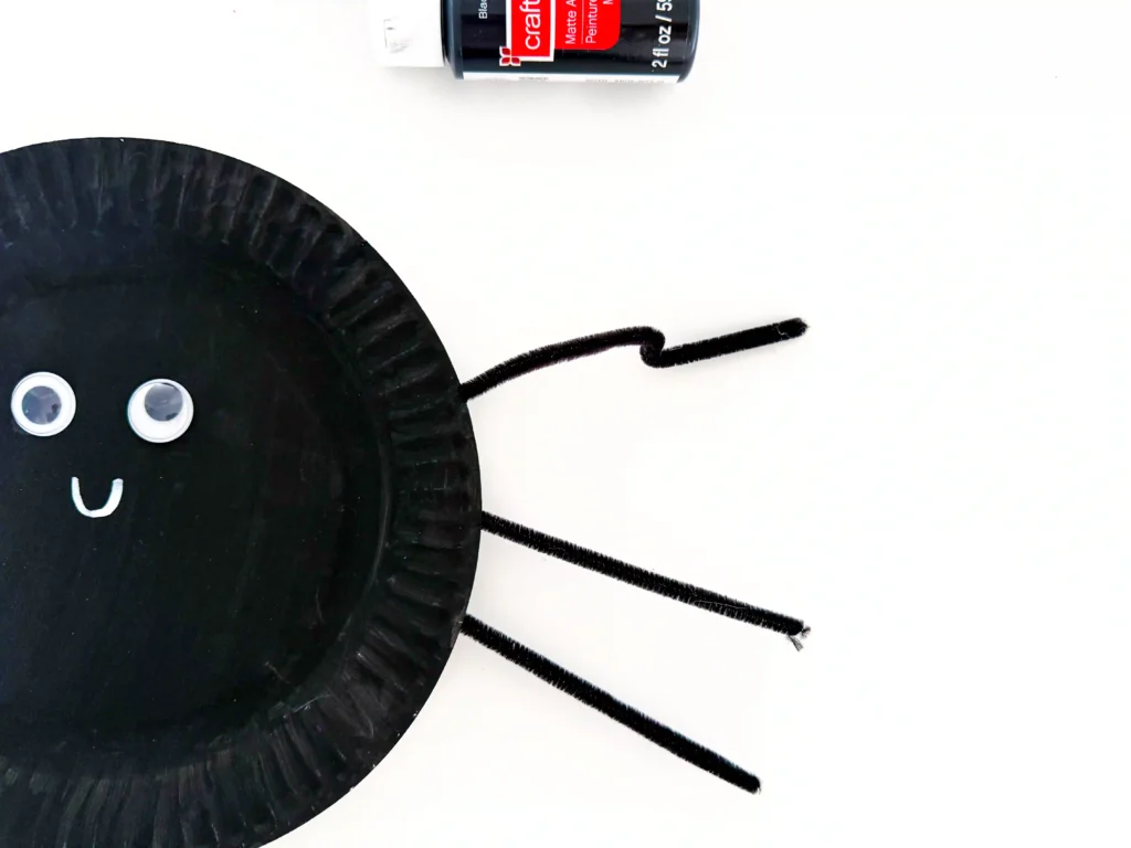 googly eyes glued on a plate painted black with black pipe cleaner legs