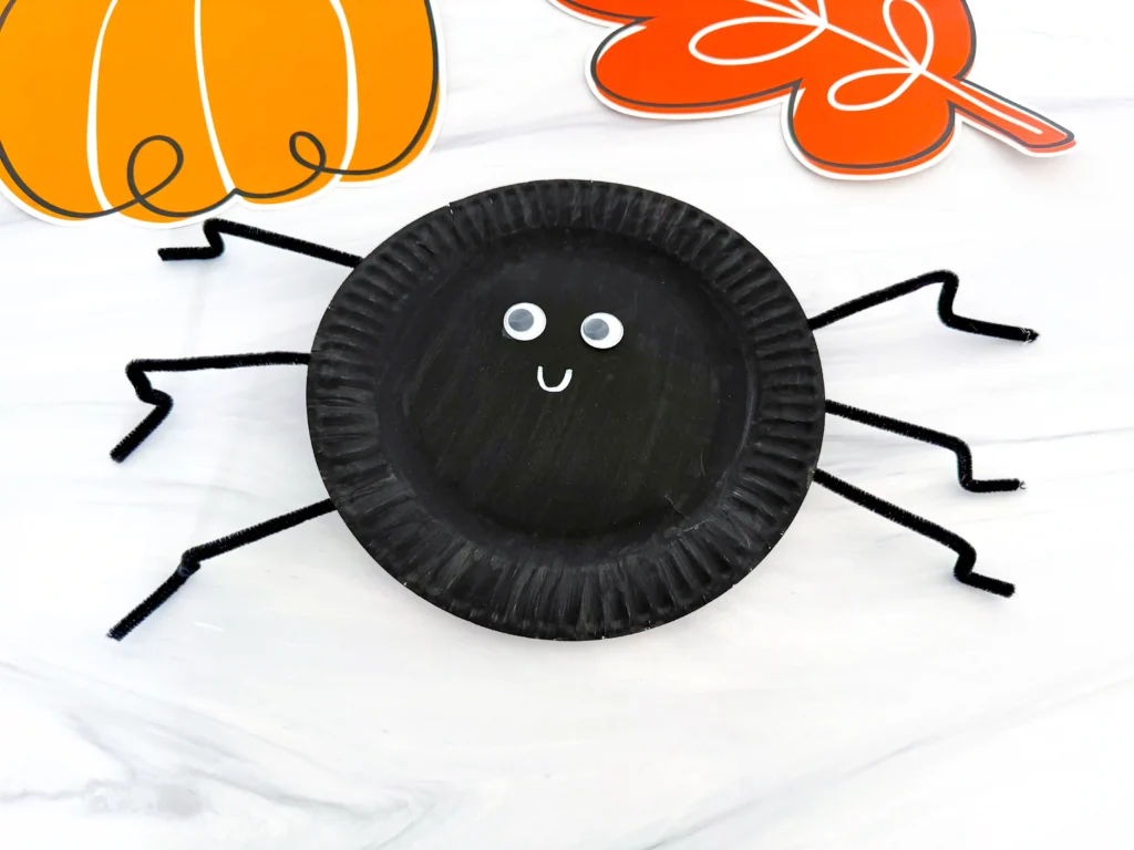 a paper plate painted black and decorated to look like a spider