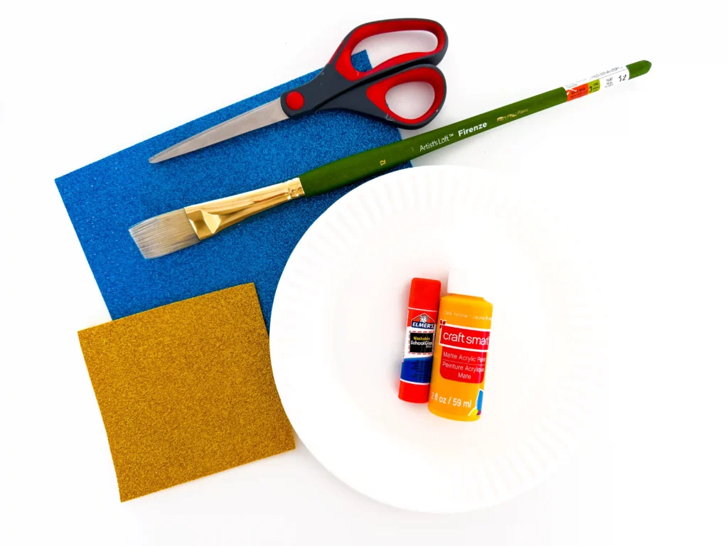 supplies for the menorah paper plate craft- scissors, paintbrush, blue and yellow glitter paper, paper plate, glue, and yellow paint