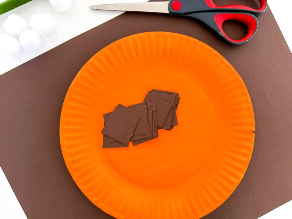a paper plate painted orange with strips of brown construction paper on it