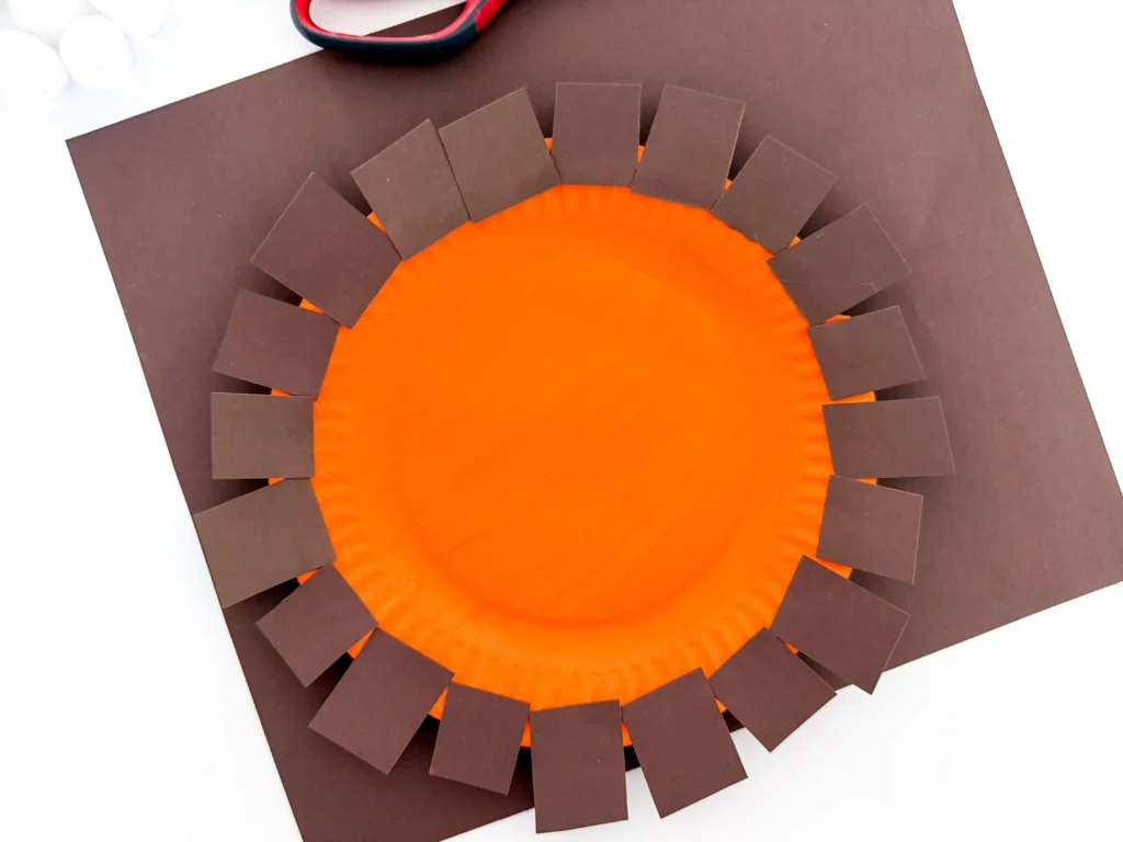 a paper plate painted orange with brown construction paper pieces on the outside edge