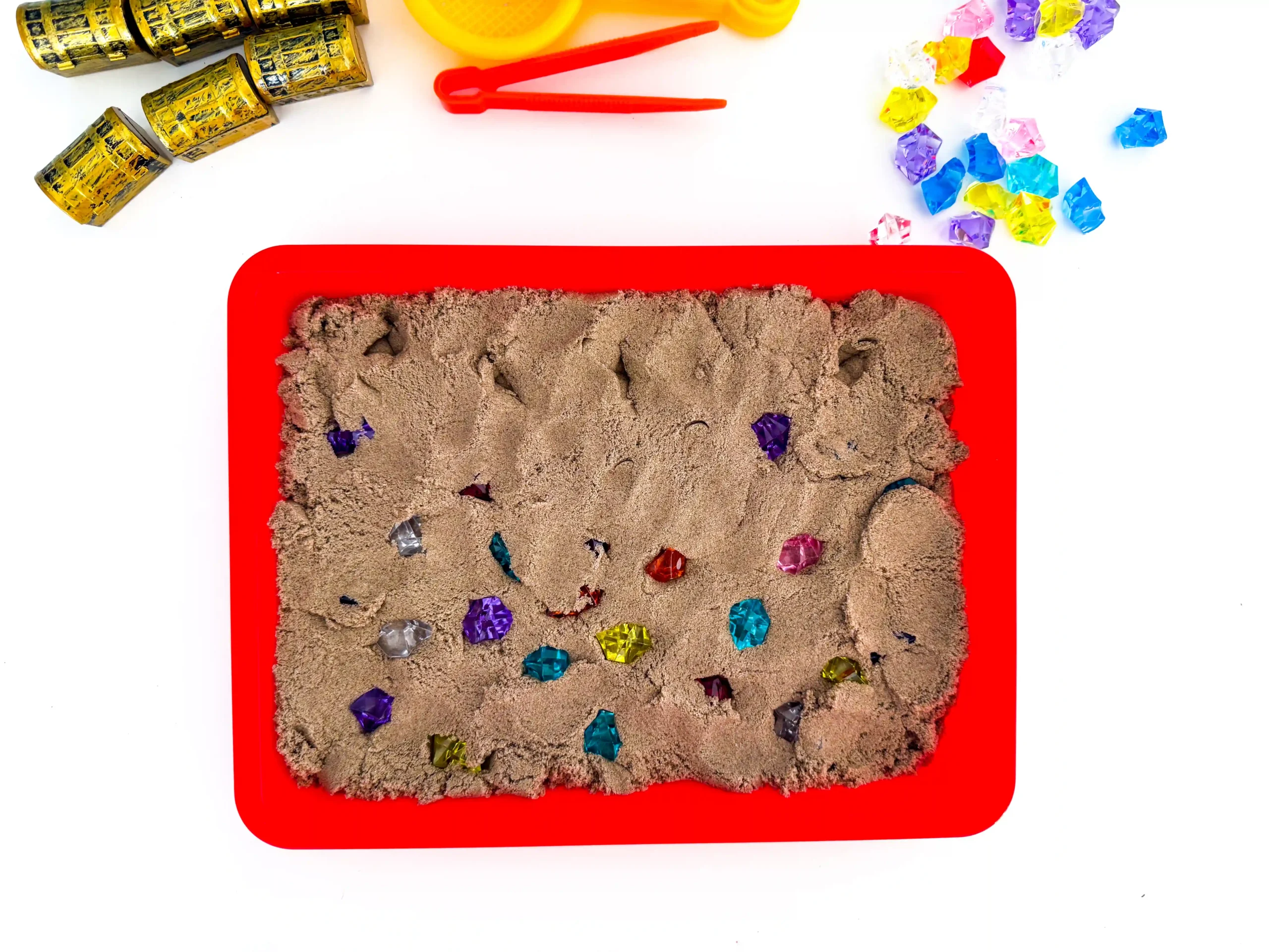 a red tray with kinetic sand and gems