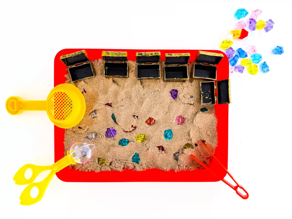 a Treasure Hunt Sensory Bin with kinetic sand, and gems in treasure chests