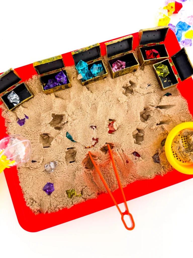 a Treasure Hunt Sensory Bin with kinetic sand, and gems in treasure chests