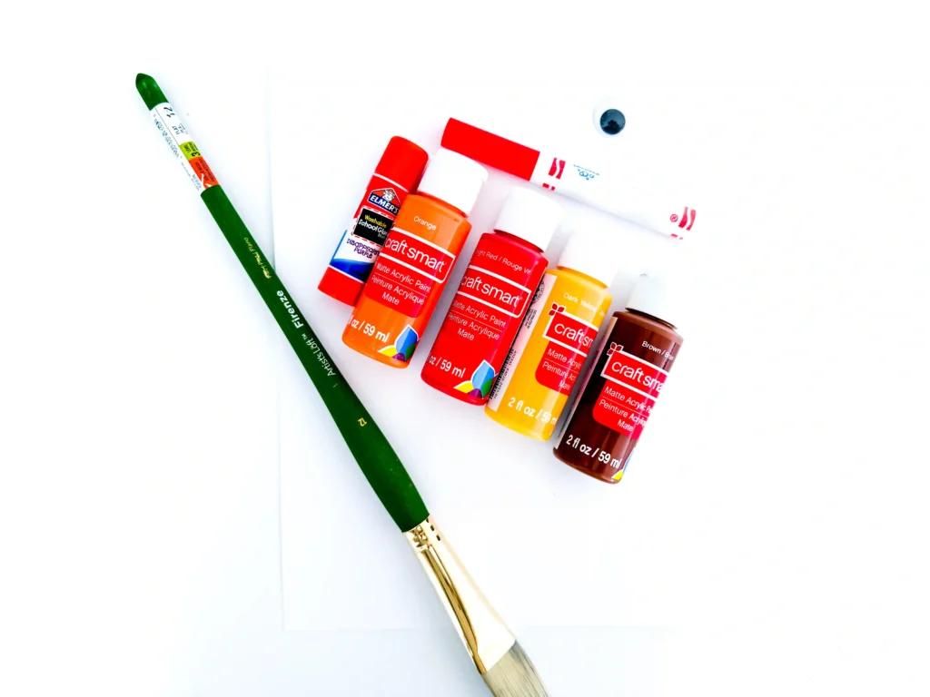 supplies for the turkey handprint craft: paper, paintbrush, glue, googly eye, red marker, red, yellow, orange, and brown paint