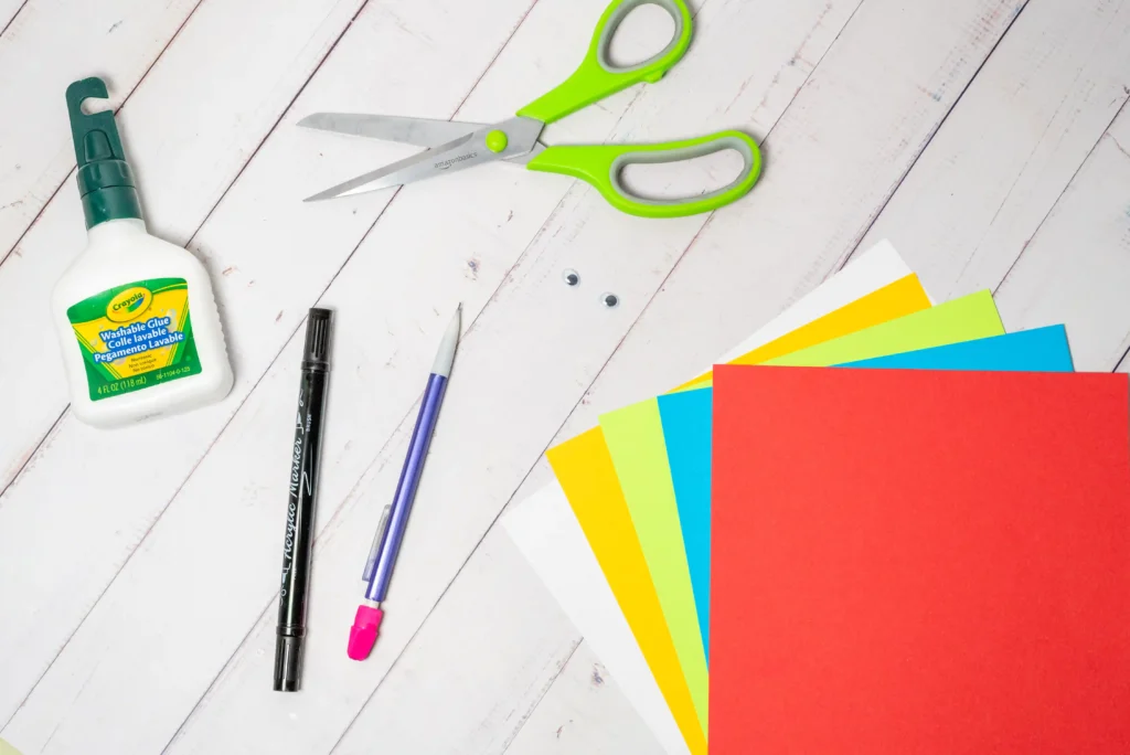 supplies for the parrot handprint craft: colored construction paper, glue, scissors, a black marker, and a pencil